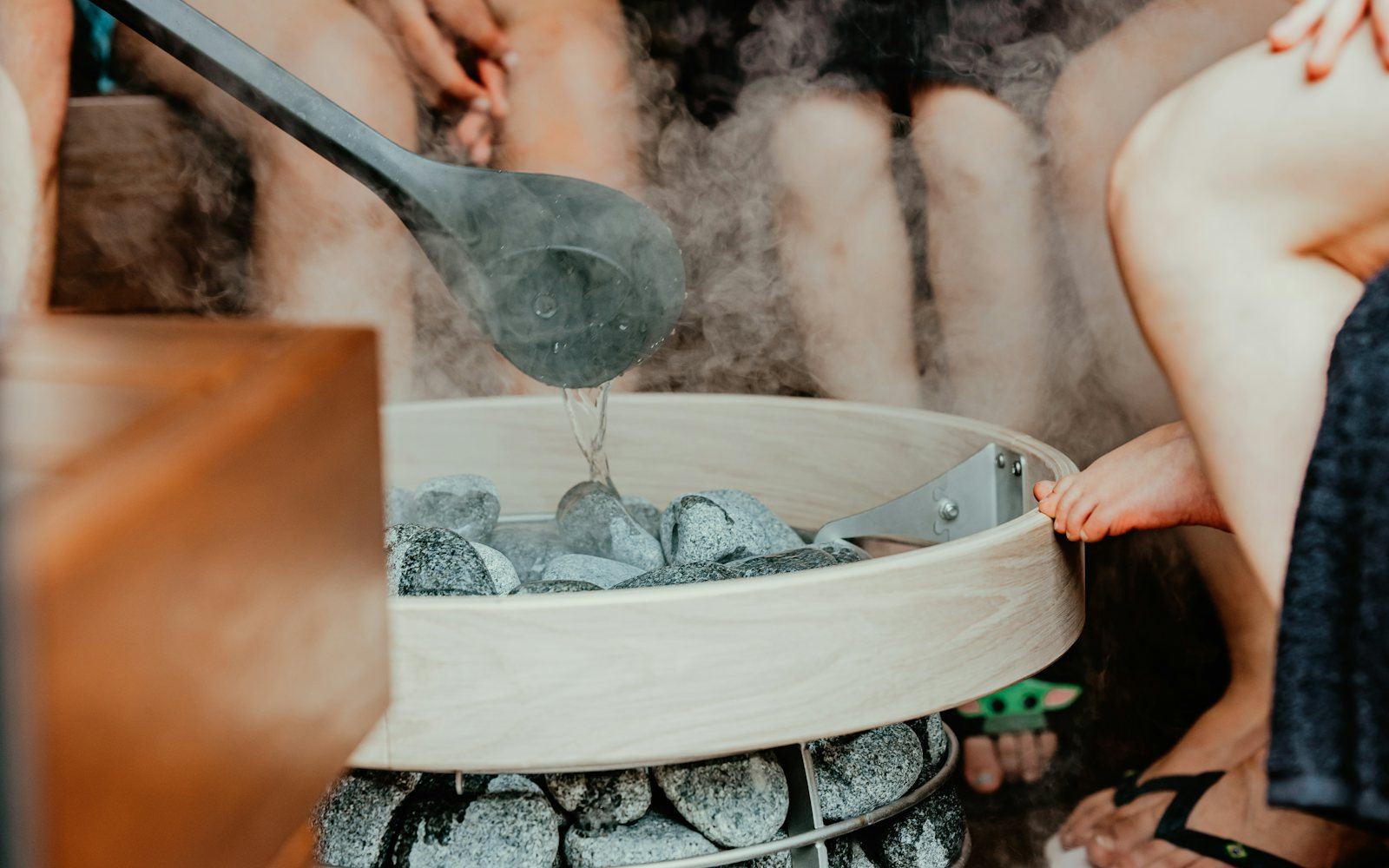 Water being ladled onto hot sauna stones, with steam rising